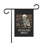 Garden flag with a skeleton and flowers design and 'Dig In & Stay Awhile' text on a black background.