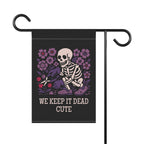 Garden flag with skeleton and flowers design and text 'WE KEEP IT DEAD CUTE' on a black background.