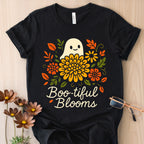 Black t-shirt with a ghost and floral design labeled 'Boo-tiful Blooms' on a wooden surface.