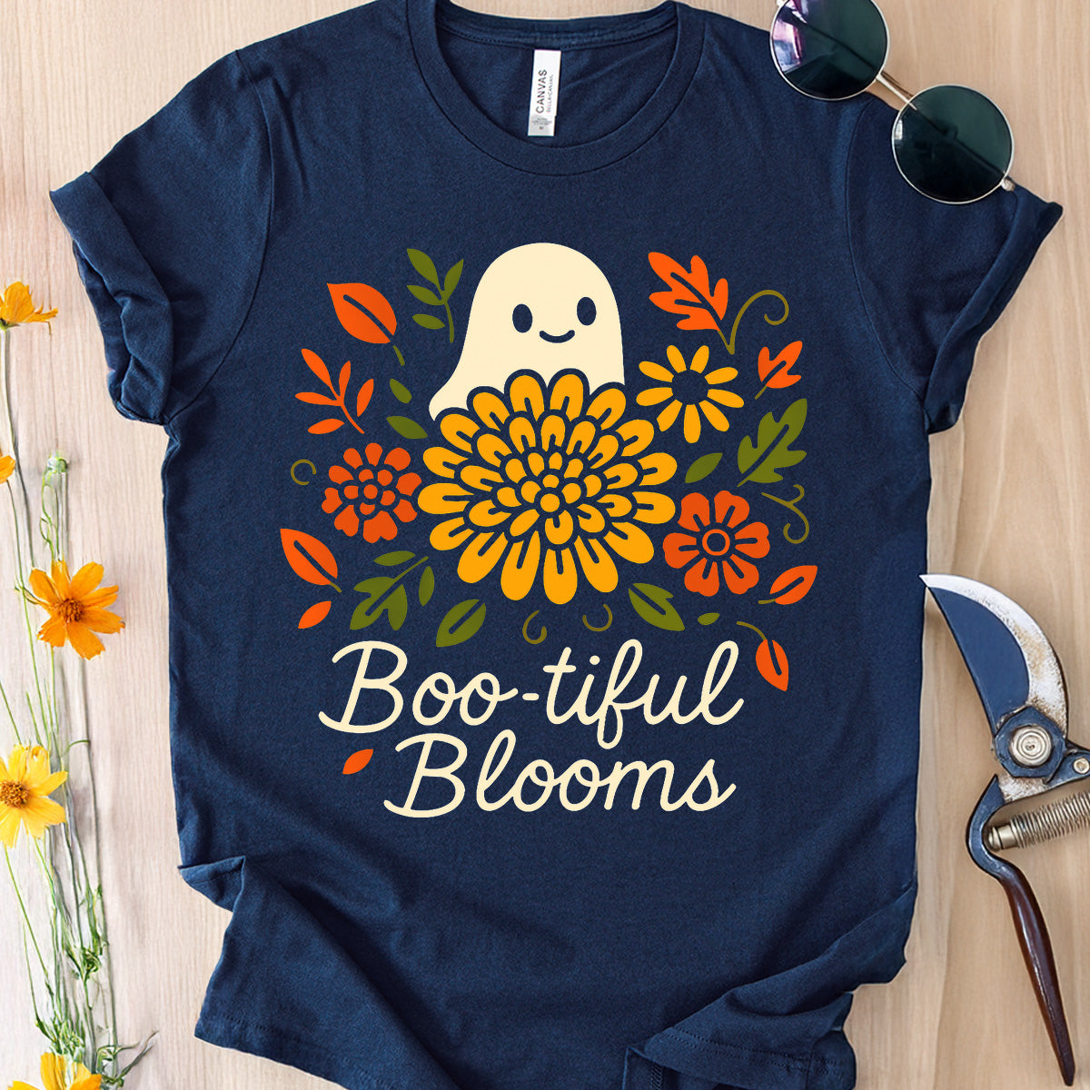 Navy blue t-shirt with a ghost and floral design labeled 'Boo-tiful Blooms' on a wooden surface.