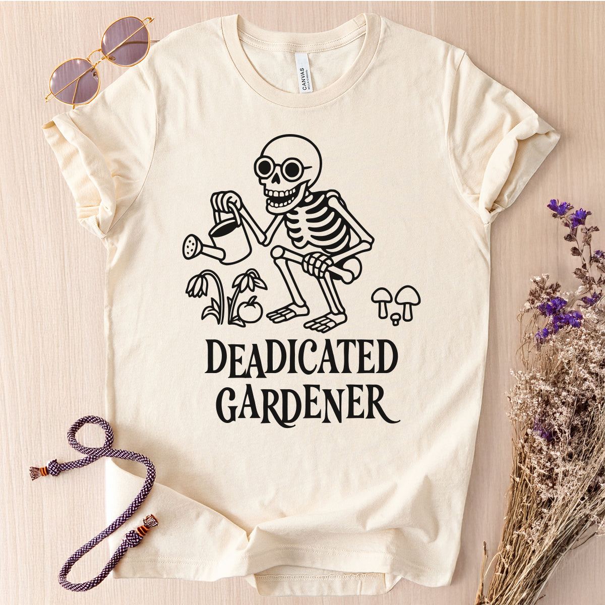 White t-shirt with skeleton graphic and 'DEADICATED GARDENER' text on a light wooden surface.