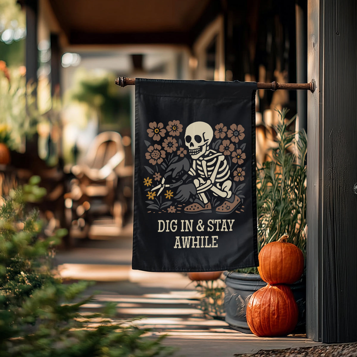 Decorative flag with skeleton design and text 'DIG IN & STAY AWHILE' hanging outdoors.