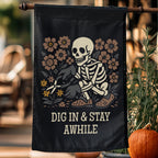 Decorative flag with skeleton and flowers design, featuring text 'DIG IN & STAY AWHILE', hanging outdoors.