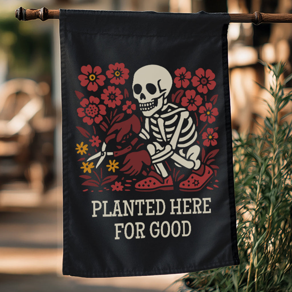 Black flag with skeleton and floral design, text 'Planted Here for Good', hanging outdoors.