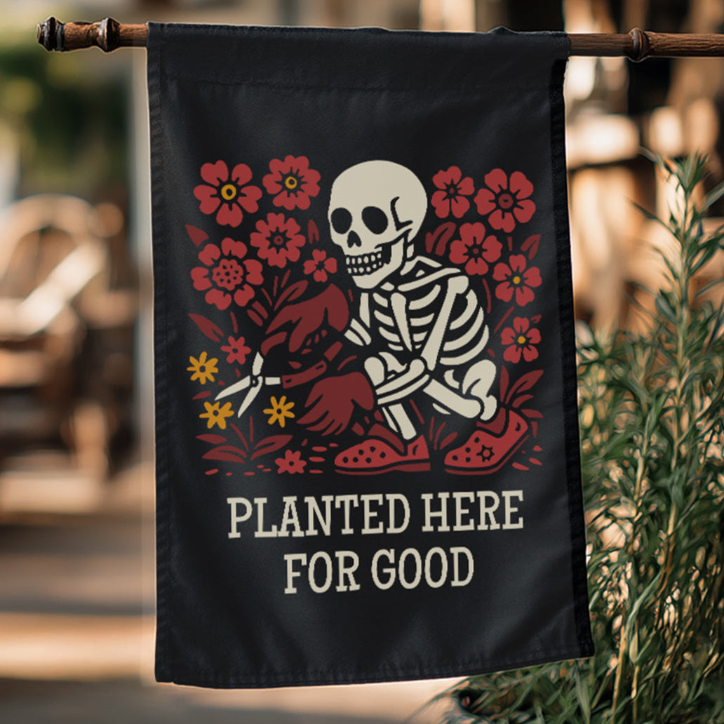 Black flag with skeleton and floral design, text 'Planted Here for Good', hanging outdoors.