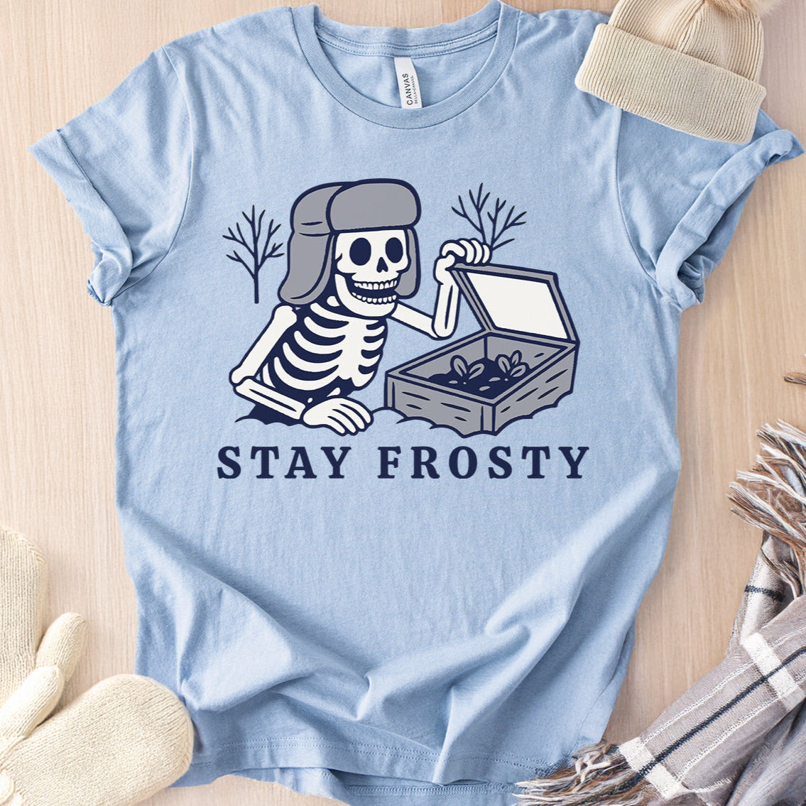 Light blue t-shirt with skeleton graphic and 'Stay Frosty' text on a wooden surface.