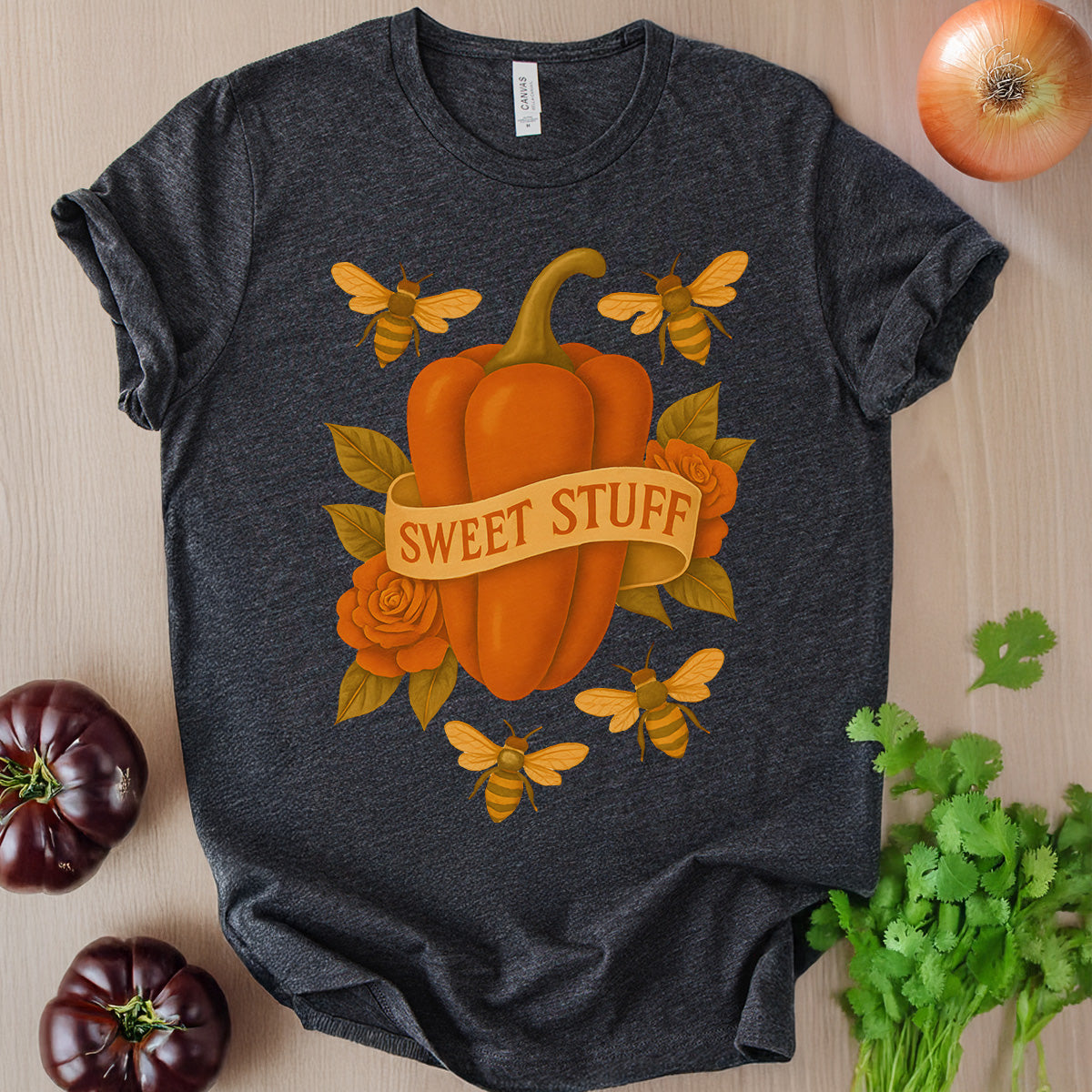 Dark gray t-shirt with a pumpkin and 'Sweet Stuff' design, surrounded by pumpkins and herbs on a wooden surface.