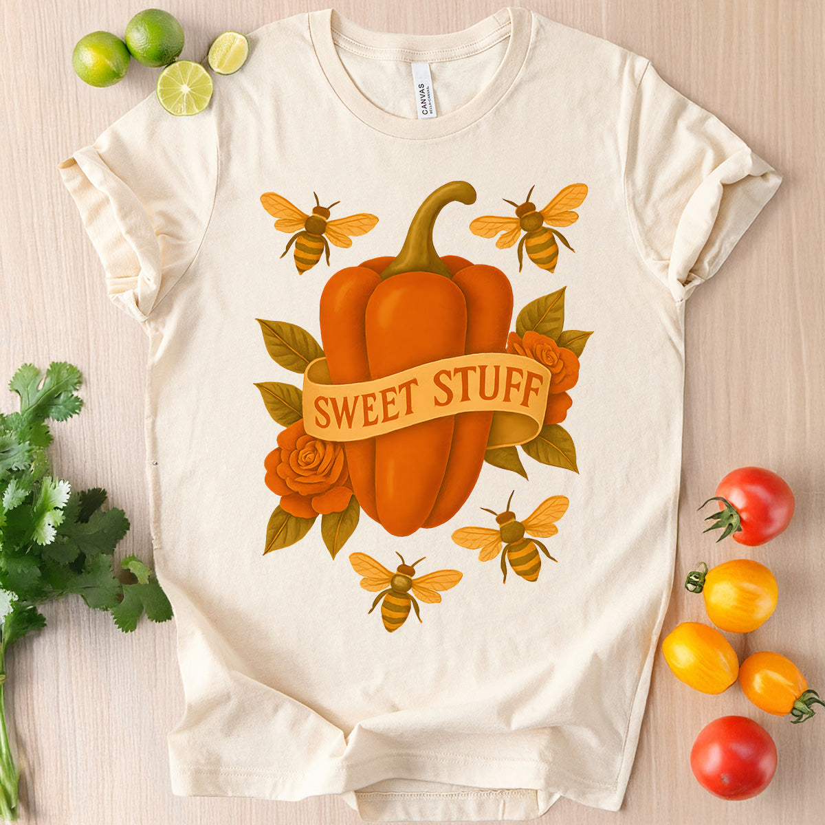 White t-shirt with a pumpkin and bee design on a wooden surface with vegetables.