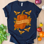 Navy blue t-shirt with a pumpkin and bee design on a wooden surface with vegetables.