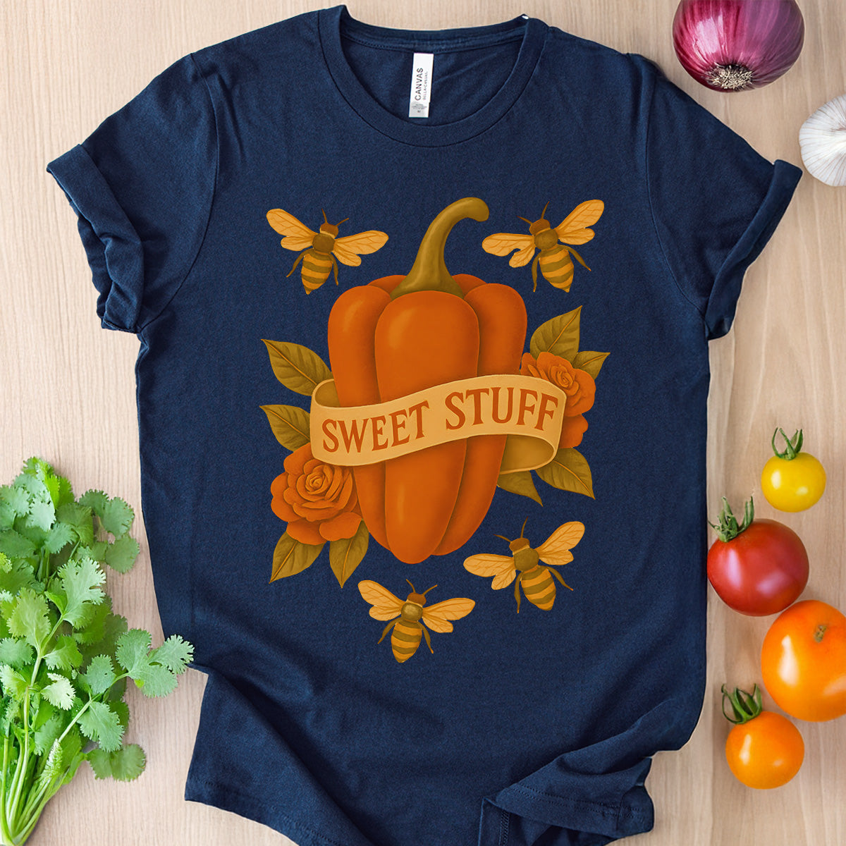 Navy blue t-shirt with a pumpkin and bee design on a wooden surface with vegetables.
