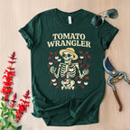 Green t-shirt with 'Tomato Wrangler' design on a wooden surface with gardening tools and flowers.