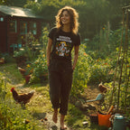 Woman walking in a garden with chickens, wearing a 'Tomato Wrangler' t-shirt.