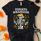 Black t-shirt with 'Tomato Wrangler' skeleton design on a wooden surface with flowers and gardening tools.
