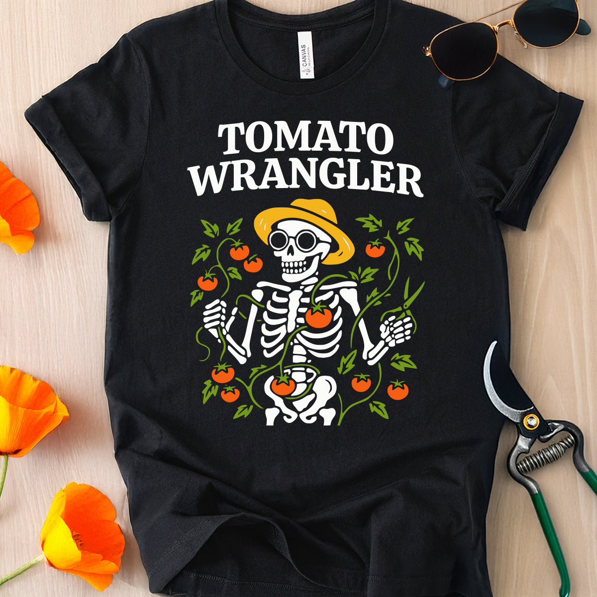 Black t-shirt with 'Tomato Wrangler' skeleton design on a wooden surface with flowers and gardening tools.