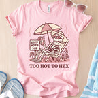 Pink t-shirt with skeleton design and text 'Send More Ice, Too Hot To Hex' on a wooden surface.