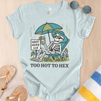 Light blue t-shirt with skeleton design and text 'Send More Ice, Too Hot To Hex' on a wooden surface.