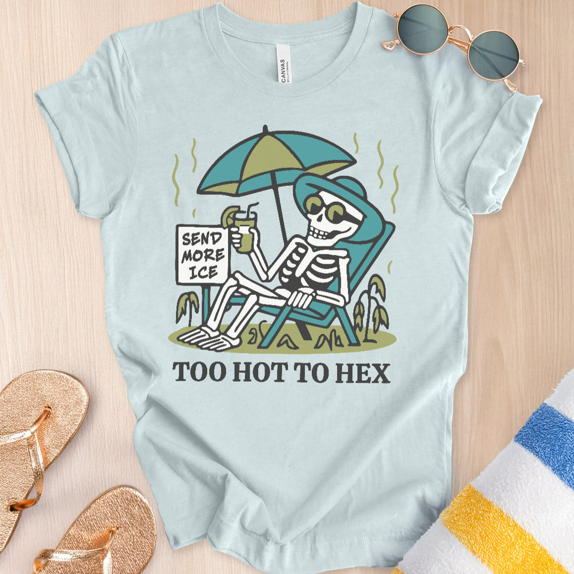 Light blue t-shirt with skeleton design and text 'Send More Ice, Too Hot To Hex' on a wooden surface.