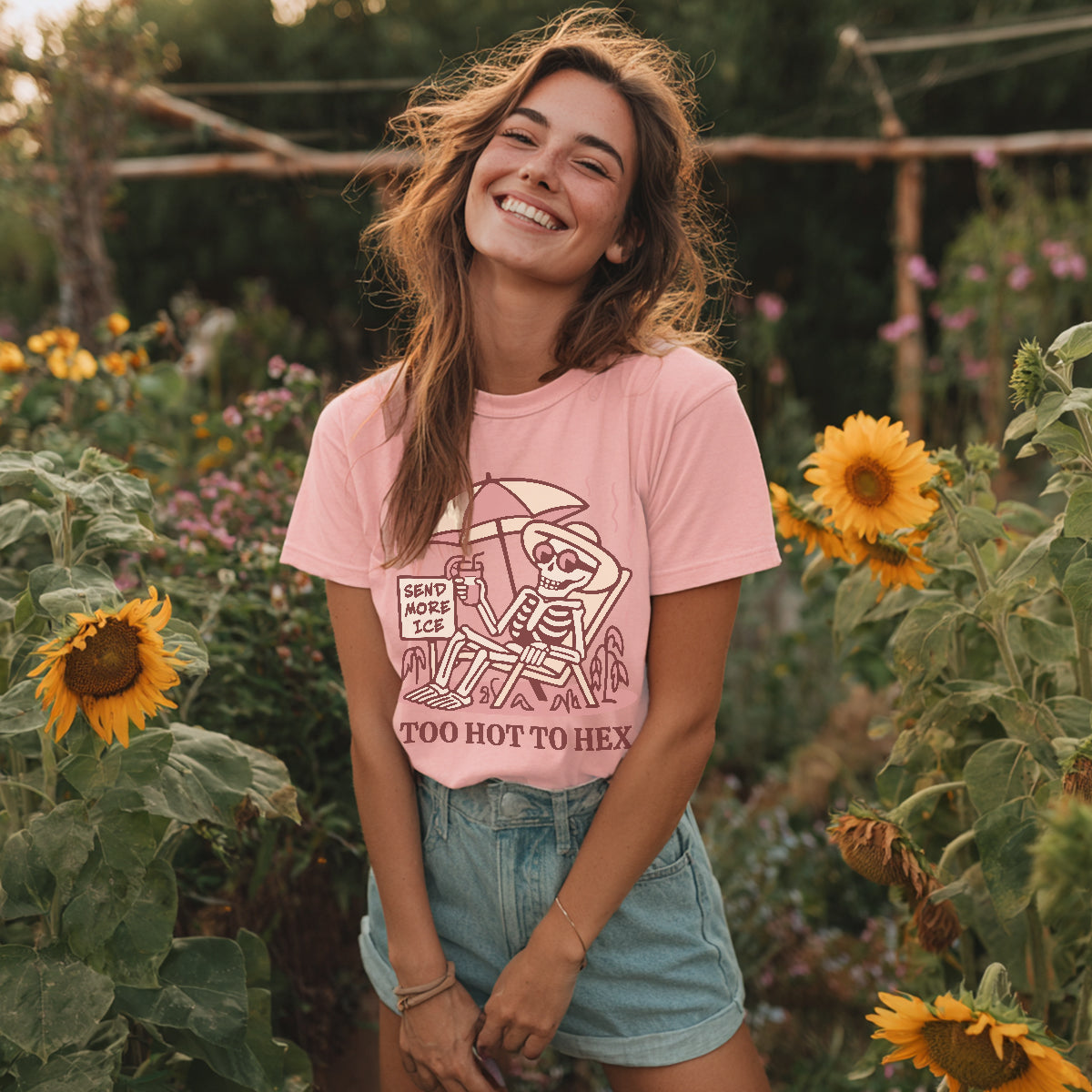 Woman in a pink t-shirt with a graphic design standing among sunflowers and other plants.