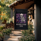 Decorative garden flag with skeleton and flowers design hanging on a wooden post outdoors.