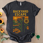 Dark gray t-shirt with 'Backyard Escape' graphic design on a wooden surface with sunflowers and sunglasses.