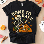Black t-shirt with skeleton design and 'Bone to Rake' text on a wooden surface with Halloween decorations.