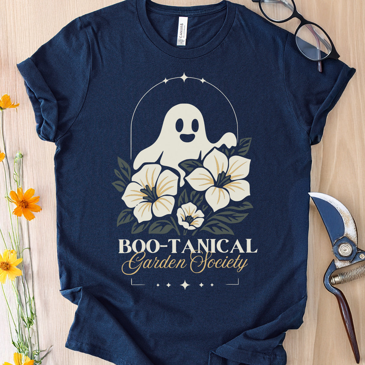 Navy blue t-shirt with a ghost and floral design on a wooden surface with flowers and scissors.